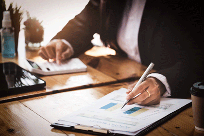 A businesswoman examines financial documents and uses a calculator to research the income affected by the coronavirus pandemic to adjust her marketing strategy.